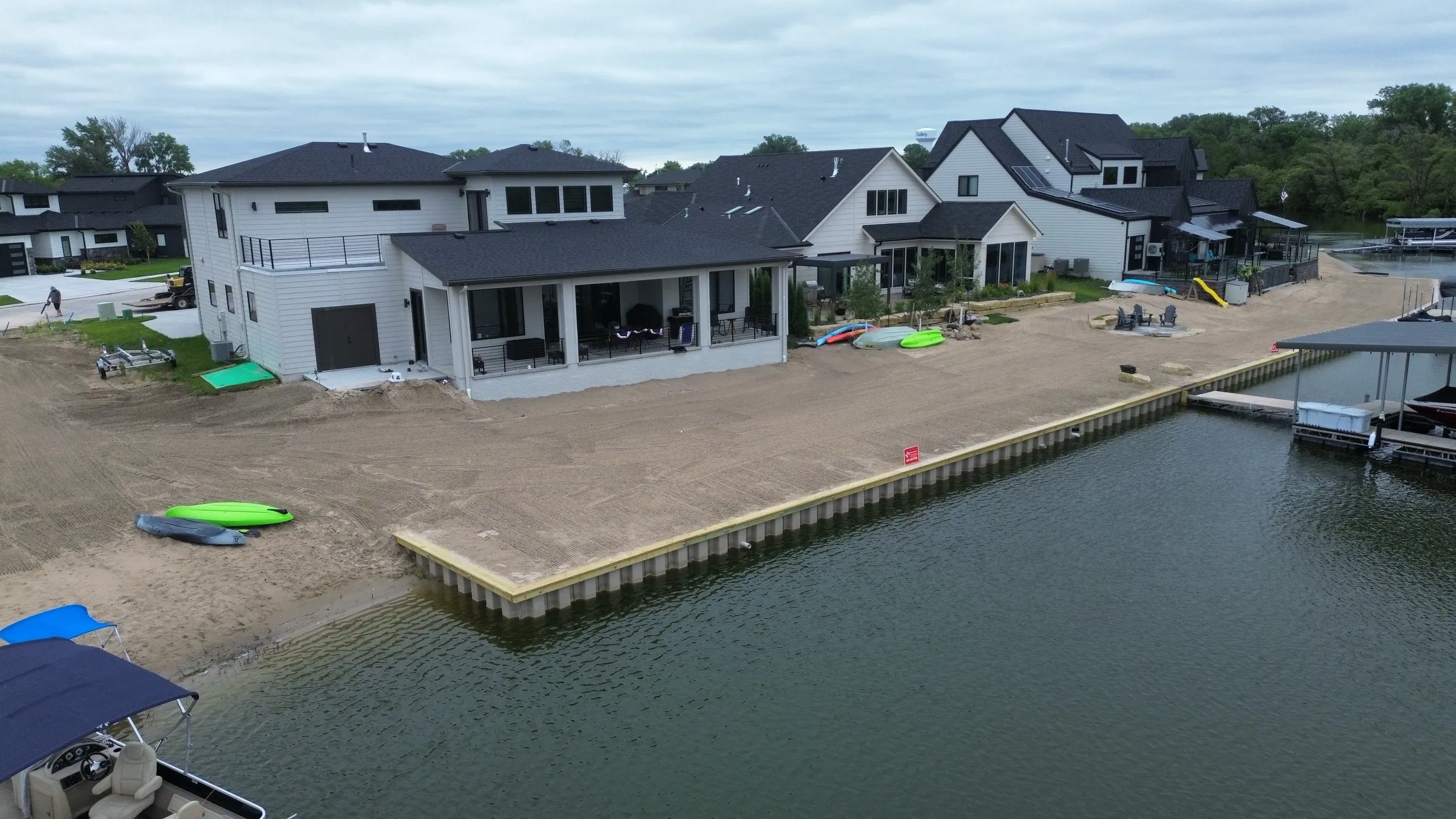 Aerial of a modern lakefront home protected by an Outback seawall, with docks and boats on a Southeast Nebraska lake